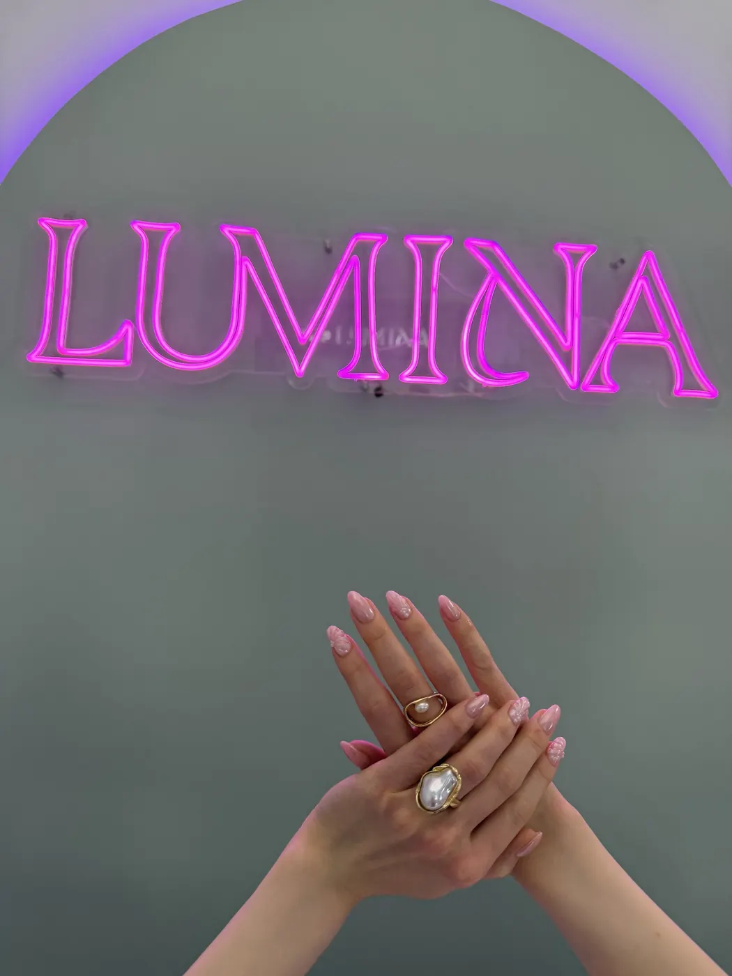 Rózsaszín mandulakörmök gyöngydíszítéssel a Lumina neonfelirat alatt